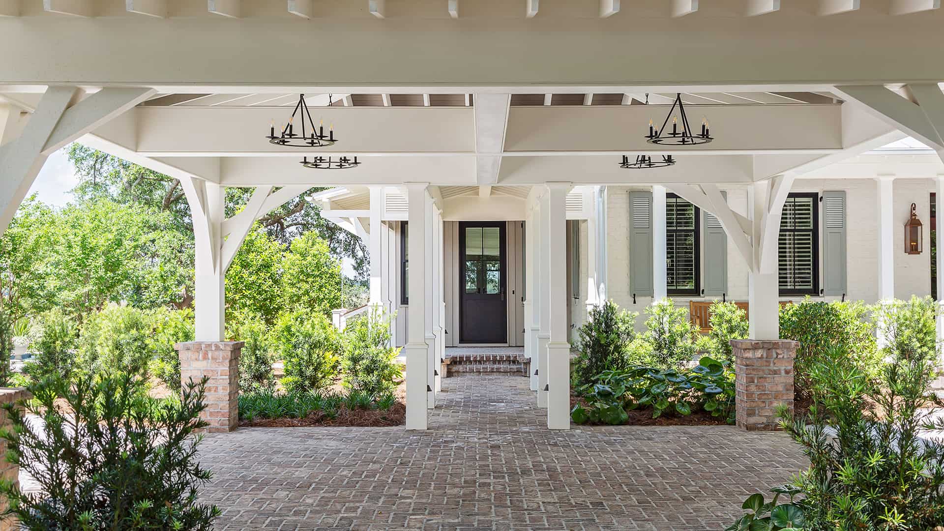 A white coastal home with a small front porch and concrete walkway, surrounded by lush greenery.