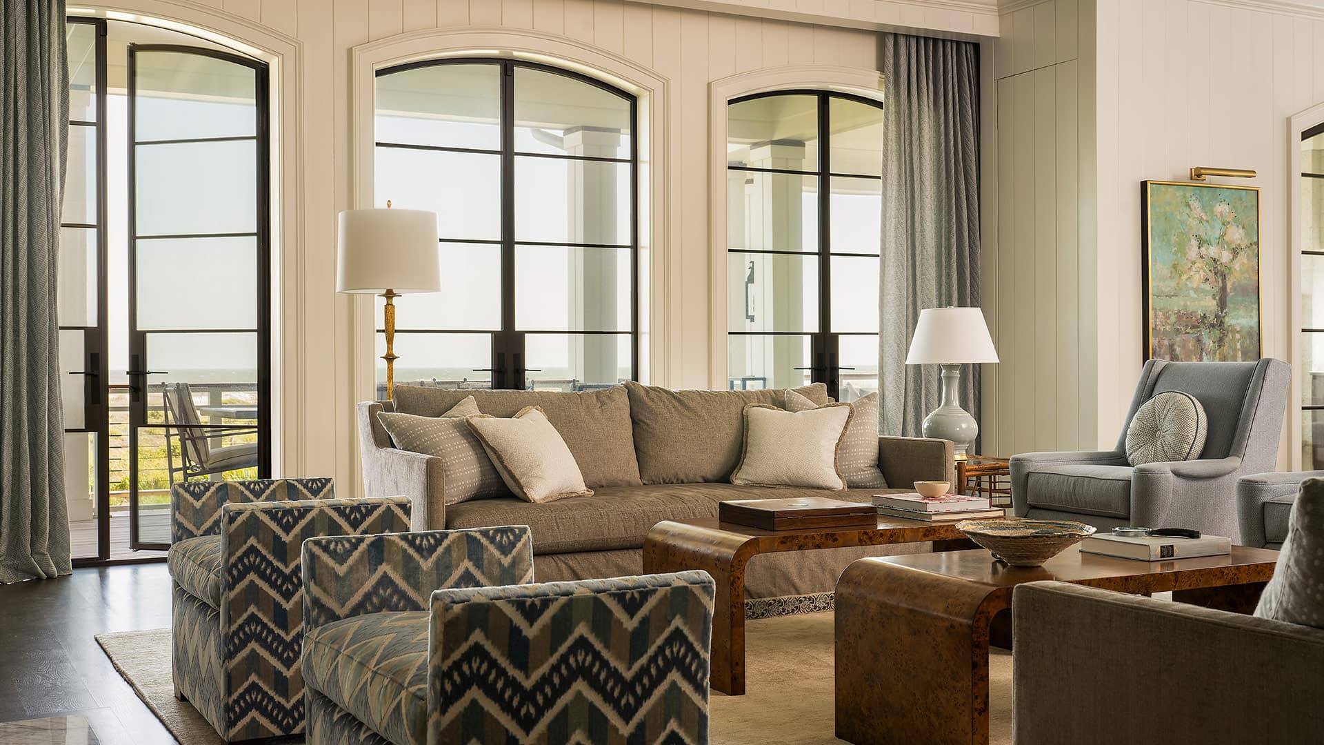 Living room with neutral furniture, large black-framed windows, and a balcony beyond.
