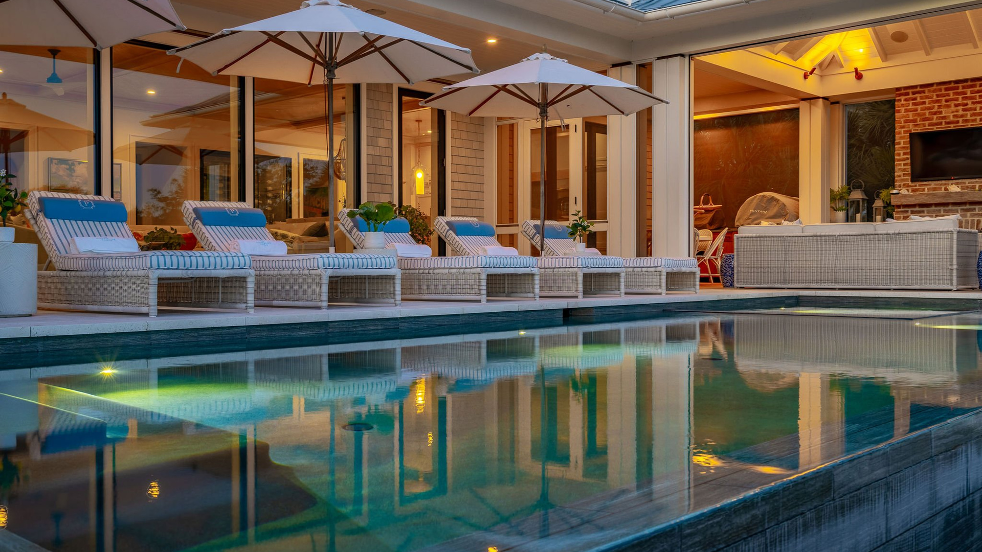 A Herlong-designed coastal home with a pool and patio, illuminated at dusk
