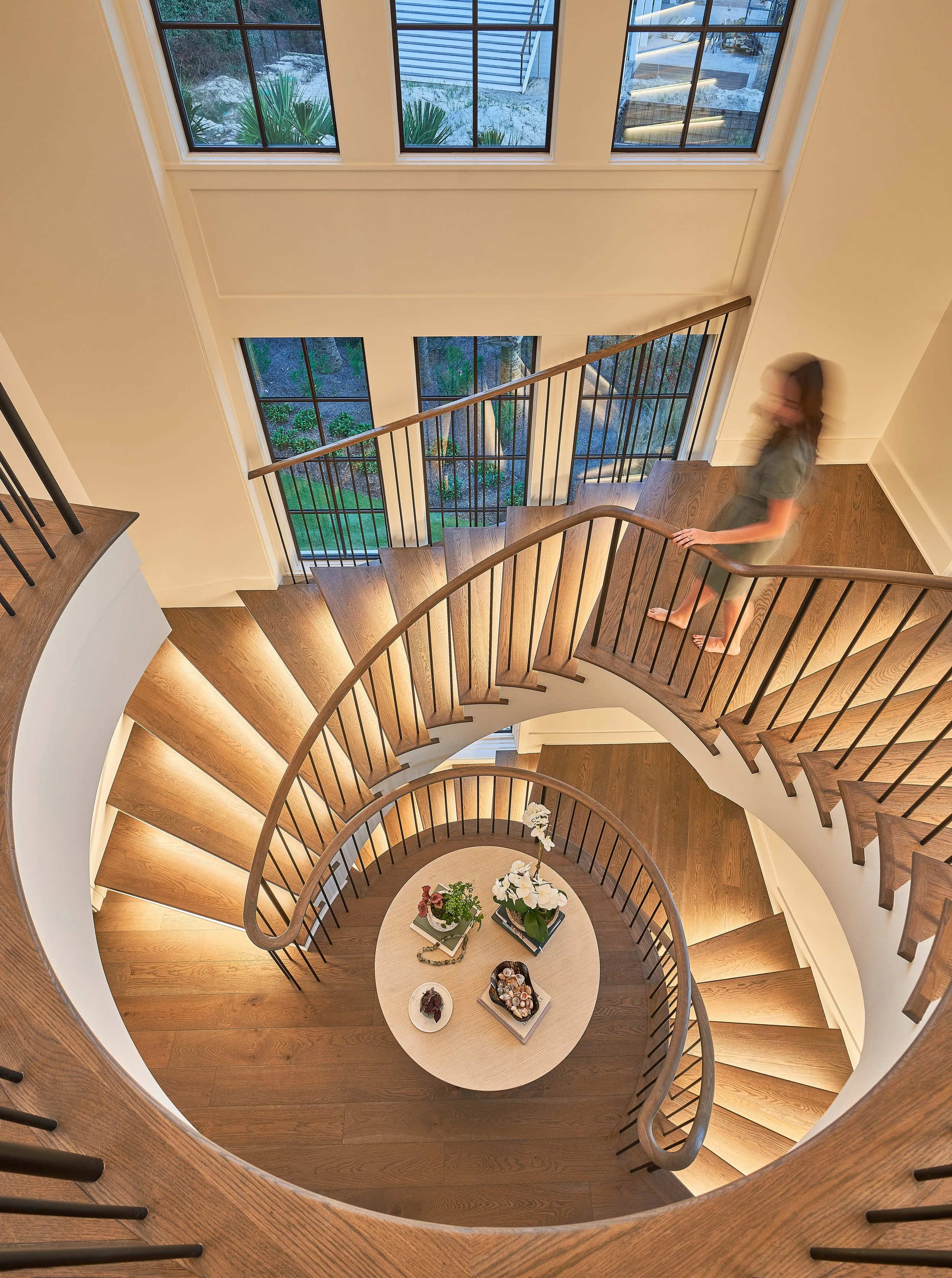Curved wooden spiral staircase viewed from above over a round entry table.