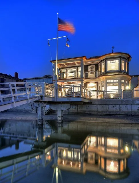 Elegant waterfront home glowing at dusk, reflected on calm water.