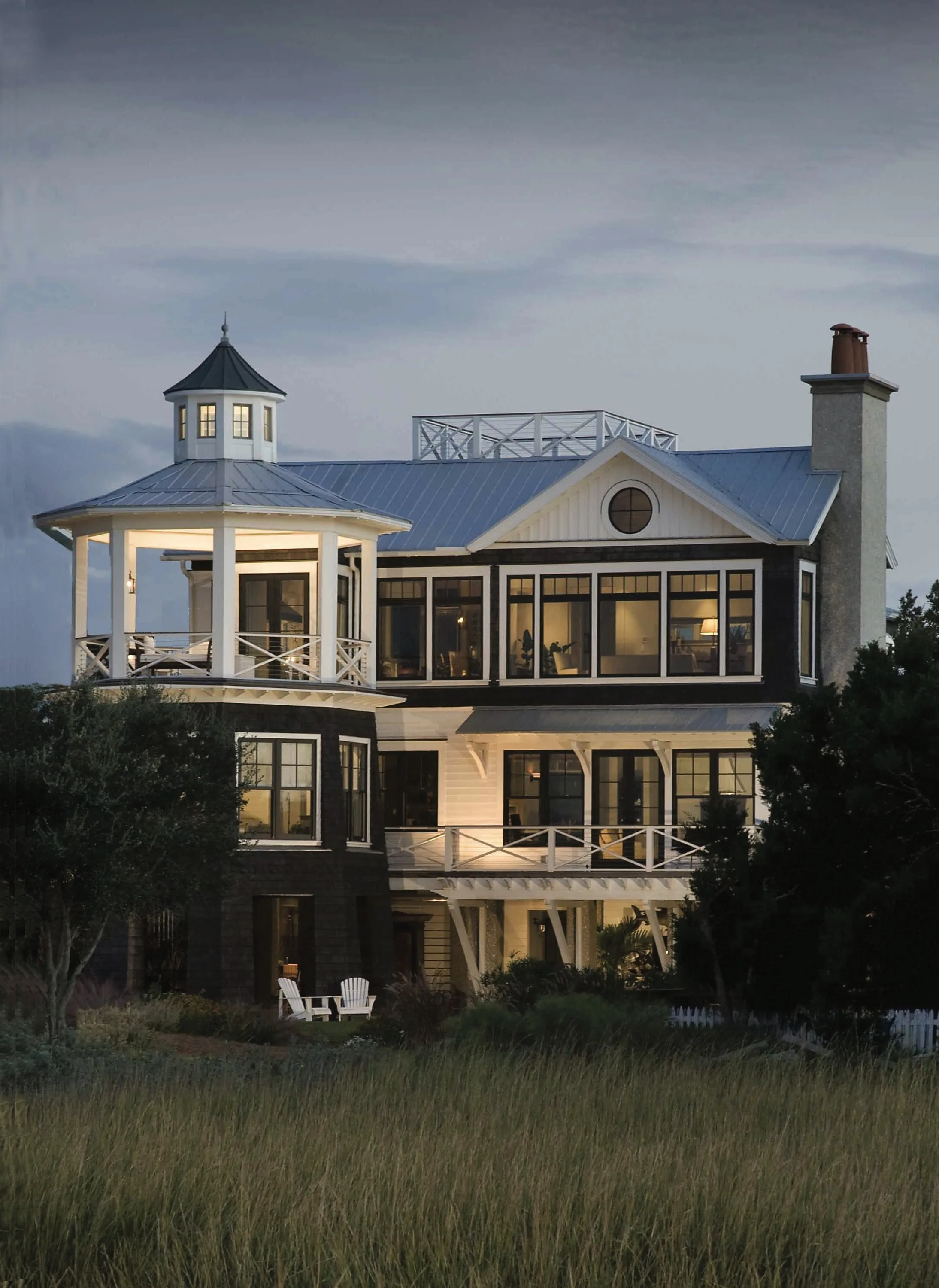 Large modern beach house with a wraparound deck and cupola, framed by trees.