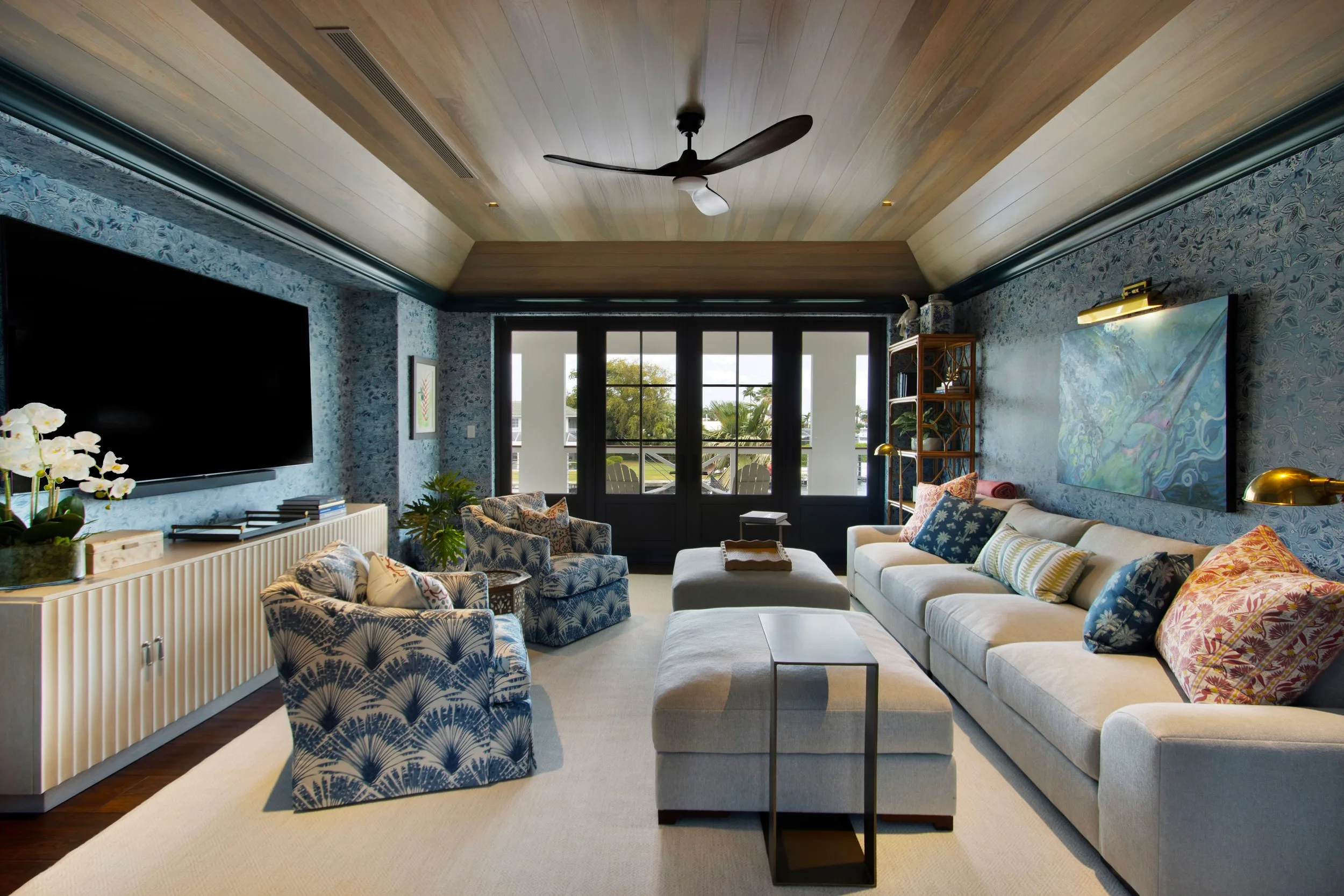Living room with blue patterned wallpaper, a white sofa with colorful cushions, and large glass doors to the outdoors.