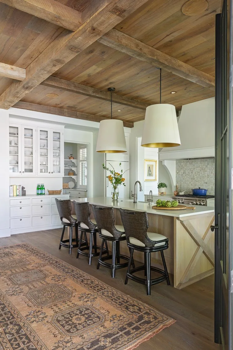 Modern farmhouse kitchen with a wooden ceiling, large pendant lights, white cabinetry, and a wicker-barstool island.